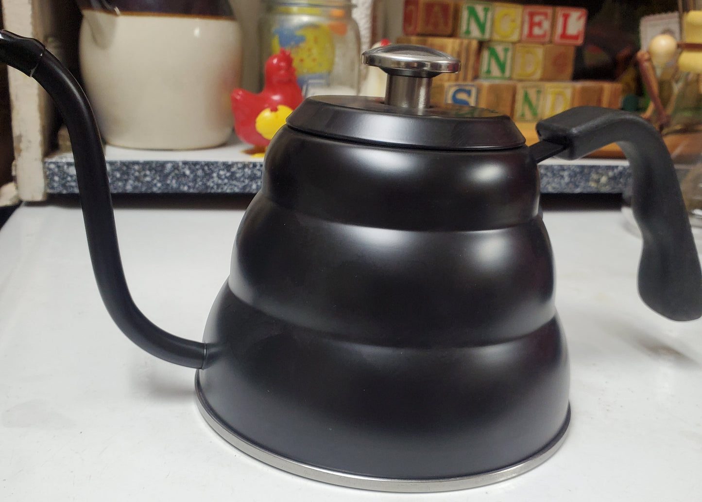 Black coffee grinder on a kitchen counter with various items in the background